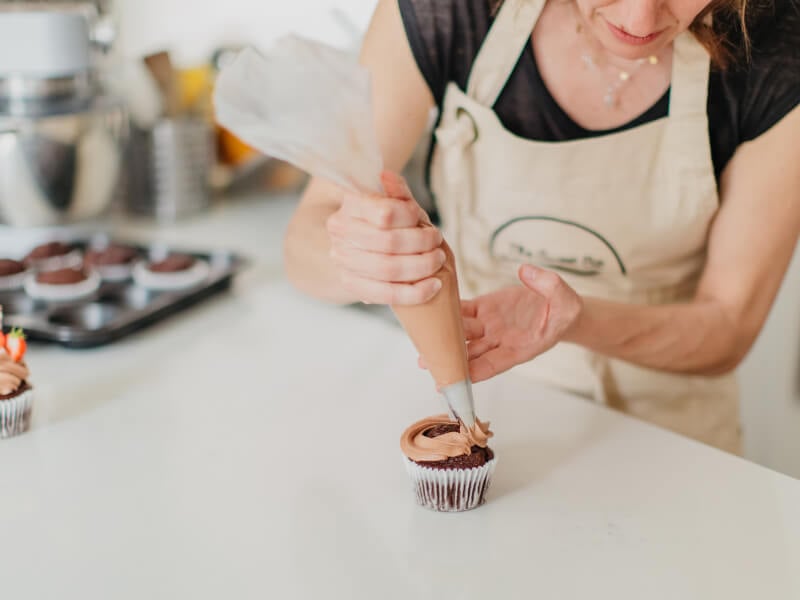A woman decorates a cupcake at a Mother's Day cake decorating class